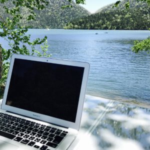 Laptop vor einer Seekulisse mit Wald im Hintergrund
